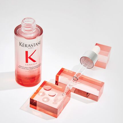 Botella de suero Kerastase Genesis anti-caida con gotero sobre bloques de colores en tonos rosas.