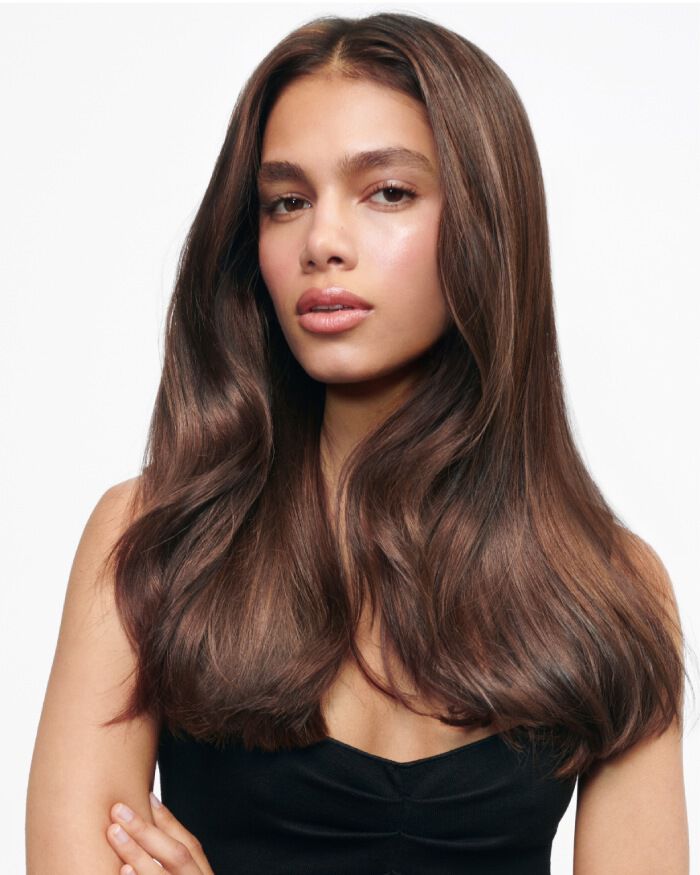 Modelo con cabello largo y ondulado, luciendo una piel radiante y una expresion serena, vestida con una blusa de tirantes negra.