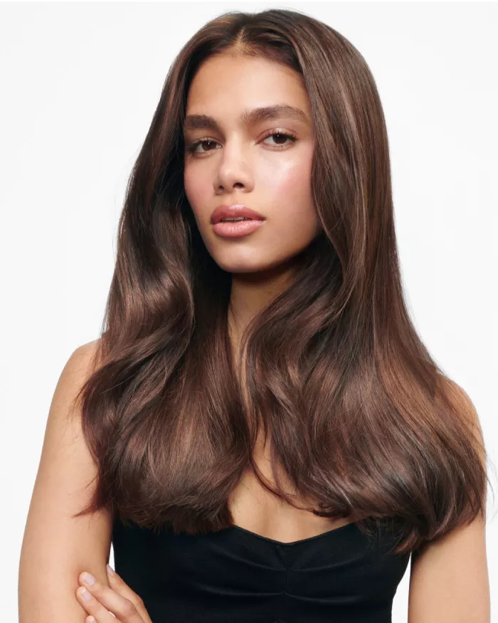 Modelo con cabello largo y ondulado, luciendo una piel radiante y una expresion serena, vestida con una blusa de tirantes negra.