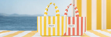 Los productos Kerastase Huile Elixir 30ml y Serum de Nuit Nutritive estan colocados sobre una toalla de playa con rayas amarillas, junto a la bolsa y el neceser Kerastase con rayas negras.