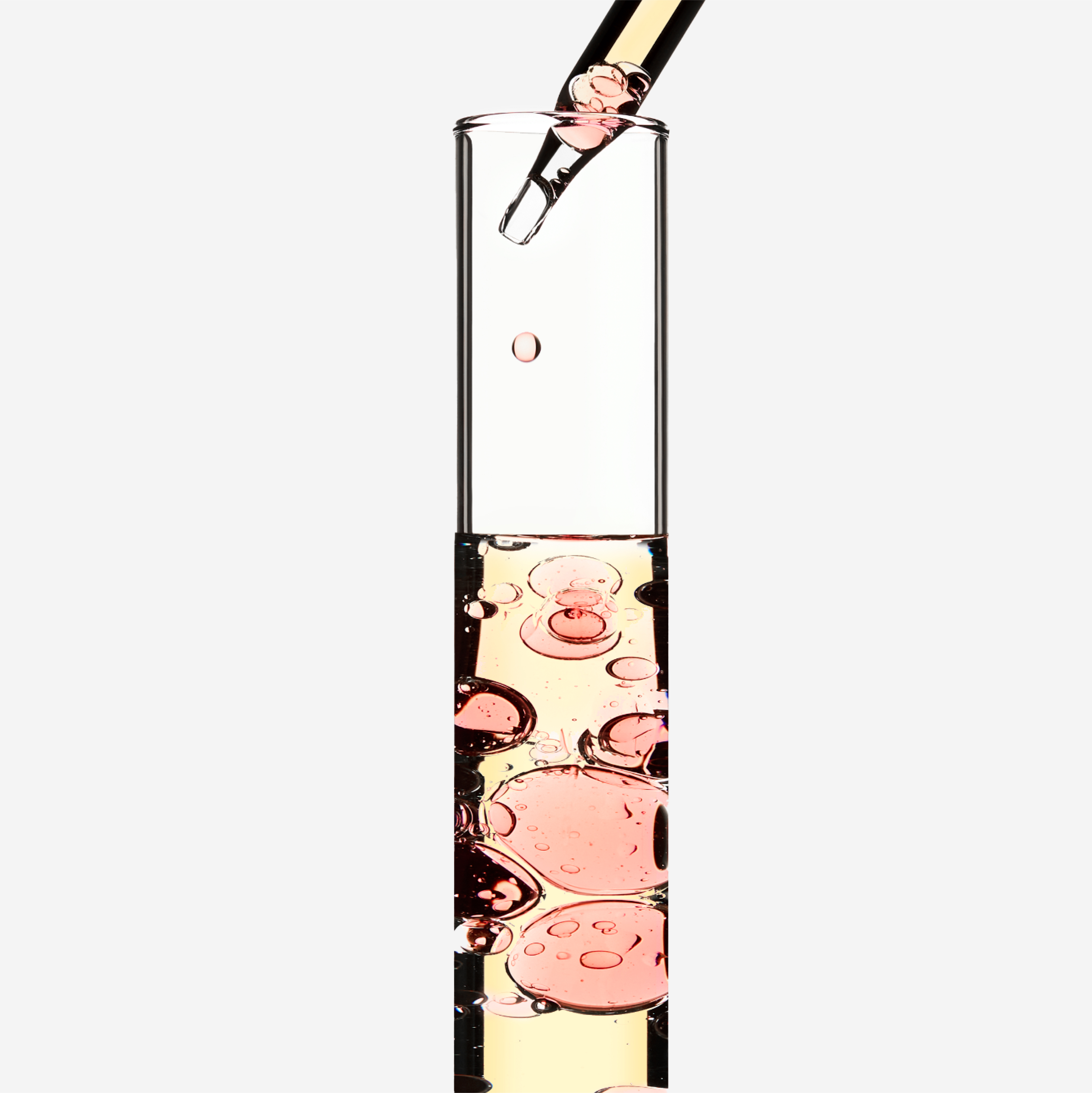 Un gotero llena un tubo de ensayo con un líquido rosa, creando burbujas y destellos en el interior.