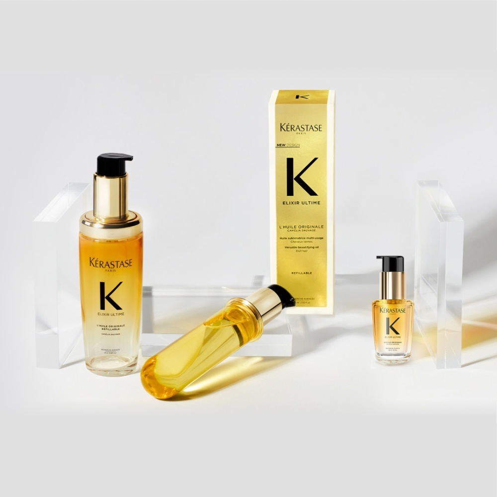 El nuevo aceite capilar Elixir Ultime, su recambio y su formato de viaje se presentan en cubos transparentes sobre fondo gris.