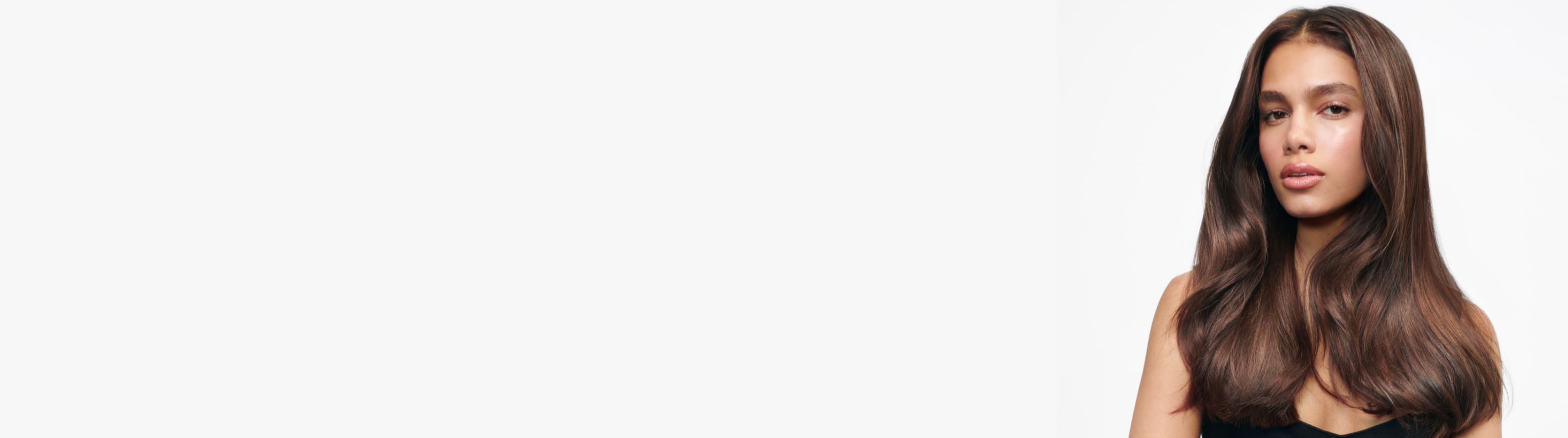 Una mujer con cabello largo, ondulado y castaño oscuro mira directamente a la cámara sobre un fondo blanco.